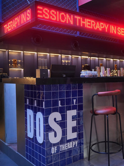 The bar at THERAPY Powai, with a red LED ticker reading THERAPY IN SESSION above it and blue tiles spelling DAILY DOSE OF THERAPY on the counter.