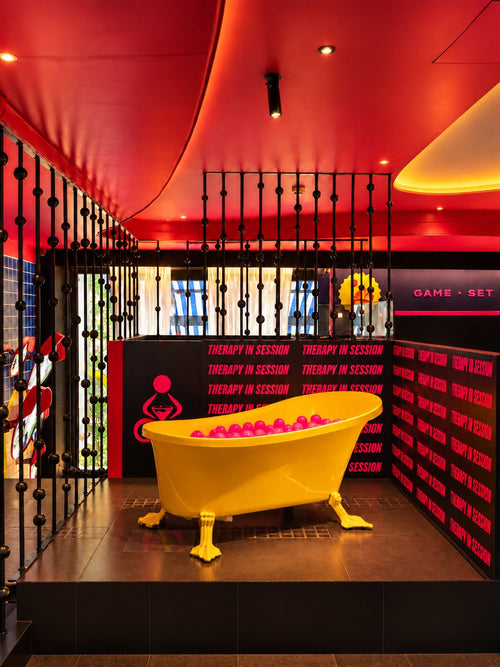 A bright yellow bathtub filled with pink balls, on a platform under a red ceiling.