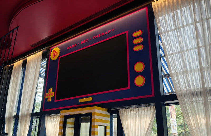 A large screen framed like a handheld games console, with the words GAME, SET, THERAPY above it.