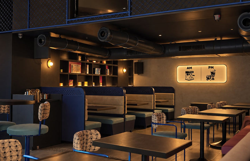 Booth seating and tables in warm light, with shelves and the AM and PM sign on the far wall.