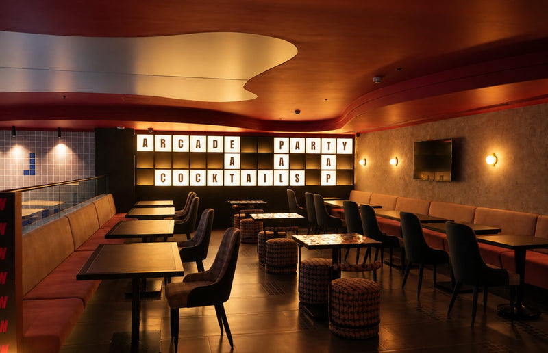 Mezzanine seating with banquettes and tables, and a lit letter wall spelling ARCADE, PARTY and COCKTAILS.