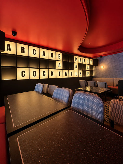 Close-up of the lit letter wall, with ARCADE, PARTY and COCKTAILS laid out like a crossword above checked chairs.