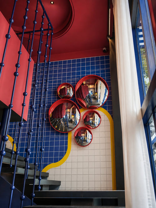 The staircase, with a cluster of round red convex mirrors on a blue and white tiled wall.